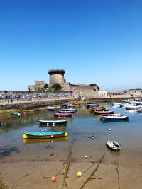 Boats moored at riverbank against clear blue sky