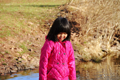 Cute girl standing by pond against grass