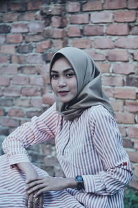 Portrait of smiling young woman standing against brick wall