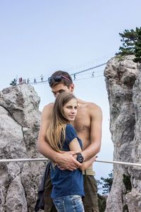 Portrait of shirtless man hugging woman while standing by rock