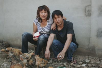 Portrait of couple by chicken on field