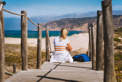 Rear view of woman sitting on wooden post