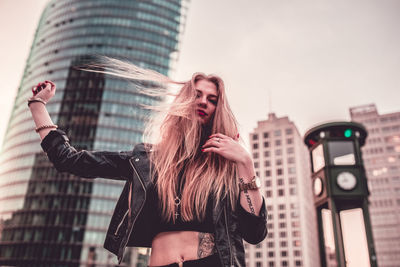 Low angle portrait of young woman standing against buildings in city