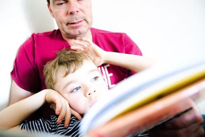 Grandfather and son holding book against white wall