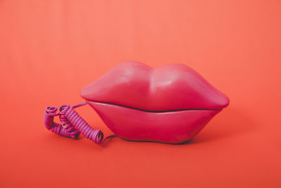 
pink vintage phone with mouth shape on orange background.