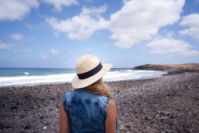 Rear view of woman standing on beach against sky