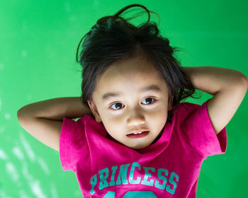 High angle view of cute girl with hands behind head lying on green background