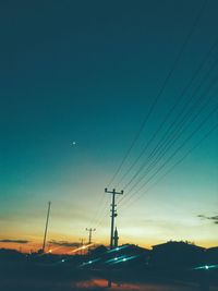 Low angle view of electricity pylons against clear sky at sunset