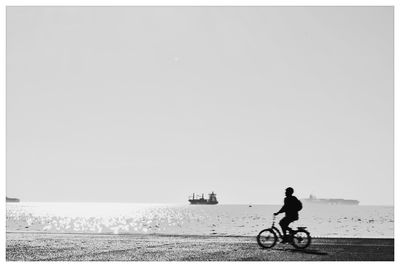 Silhouette man riding bicycle by sea against clear sky