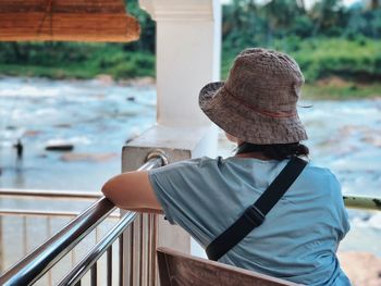 Rear view of woman looking at sea while sitting by railing