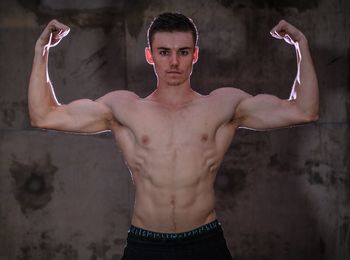 Portrait of young muscular man flexing muscles against wall