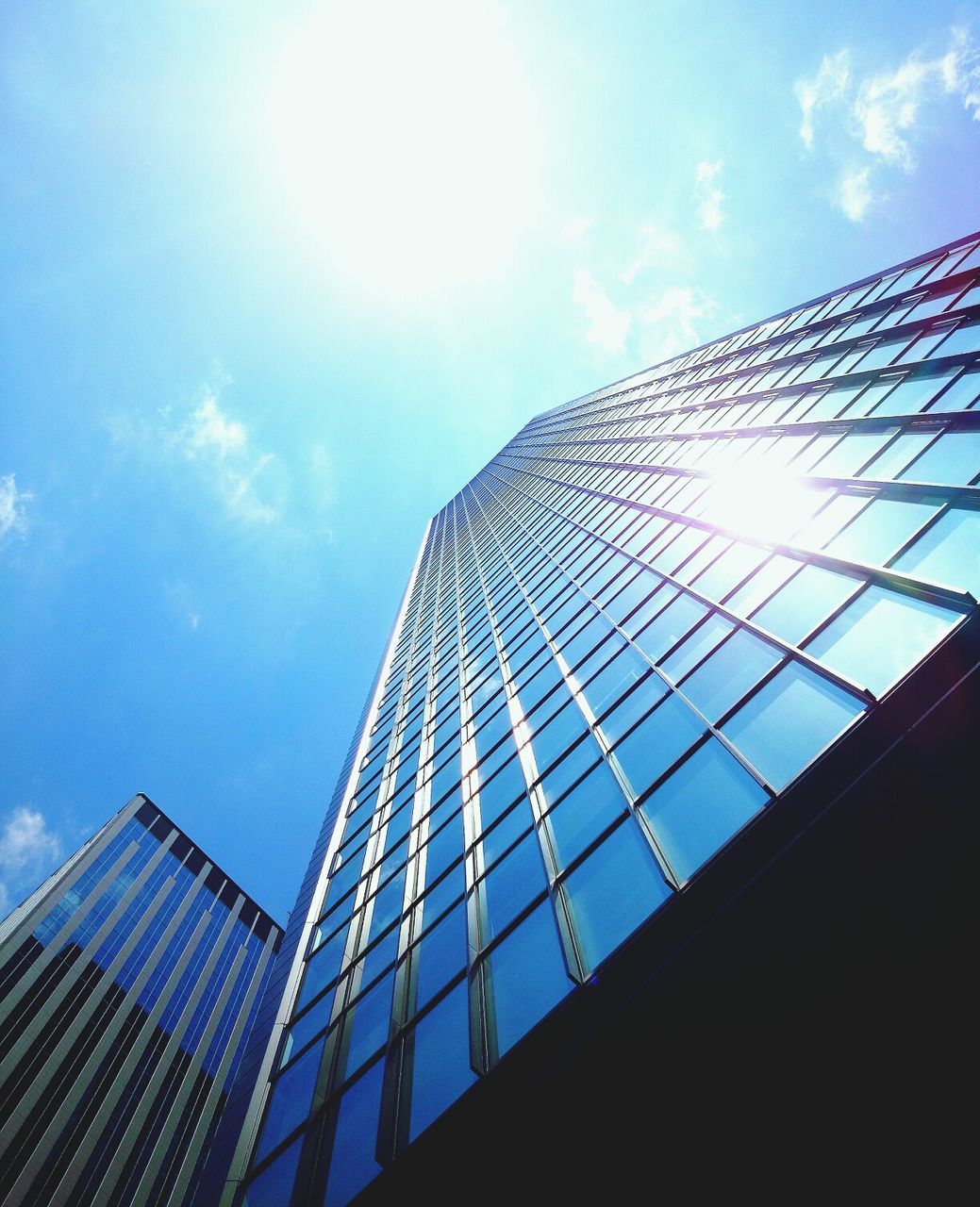 architecture, building exterior, low angle view, built structure, modern, skyscraper, office building, city, tall - high, sky, tower, reflection, glass - material, sunlight, sun, building, cloud - sky, sunbeam, blue, cloud