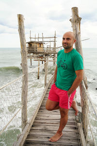Full length of bald man leaning on pier railing over sea