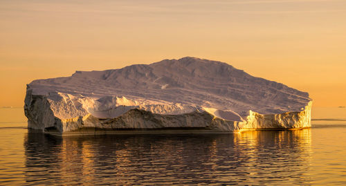 Scenic view of lake by mountain against sky during sunset