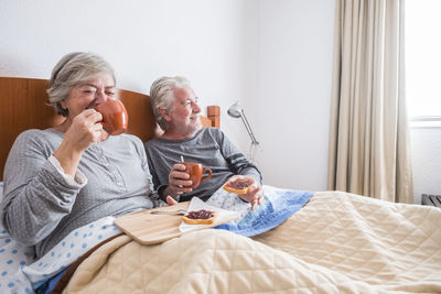Senior couple having breakfast while sitting on bed at home