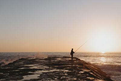 Silhouette man fishing in sea against clear sky