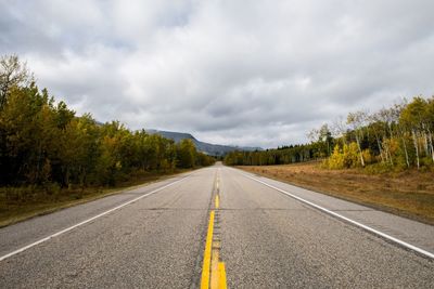 Empty road along trees and against sky