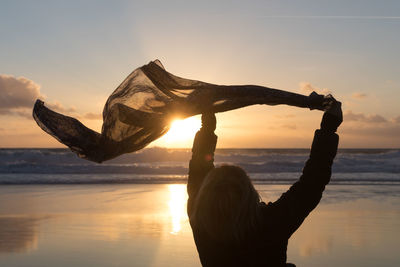 Rear view of woman holding scarf while standing at beach against sky