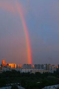 Rainbow over buildings in city against sky during sunset
