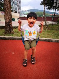 Portrait of boy with mouth open sitting on swing in park