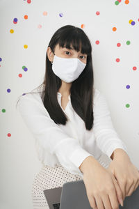 Portrait of woman wearing mask sitting against gray background