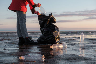 A woman cleans the bank of plastic bottles and puts the trash in a garbage bag