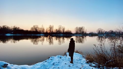 Man standing by lake against sky during winter