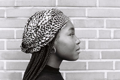 Side view of young woman with braided hair against brick wall