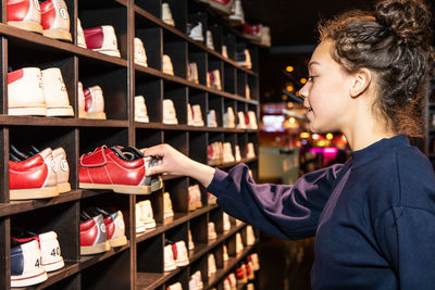 Side view of teenage girl holding bowling shoes at wooden rack