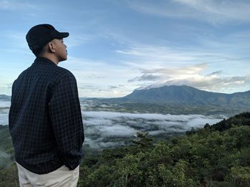 Young man looking at mountains against sky