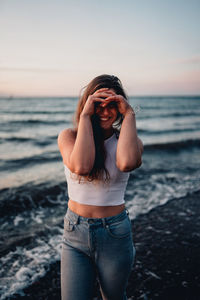 Young woman standing at beach against sky