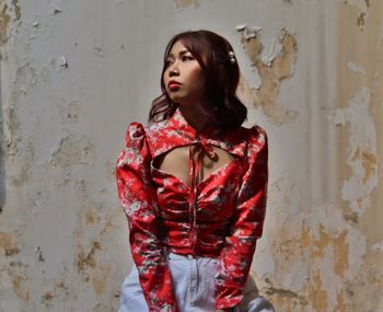 Young woman looking away while standing against wall