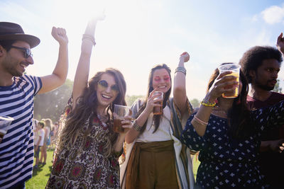 Friends holding beer in glasses while standing on grass