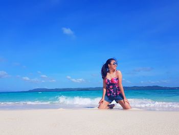 Woman kneeling on shore at beach against sky