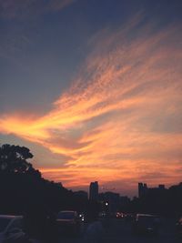 Silhouette city against dramatic sky during sunset