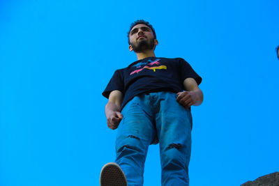 Low angle view of man looking away against blue sky
