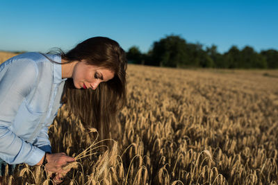 Beautiful young woman looking at wheat on field against sky