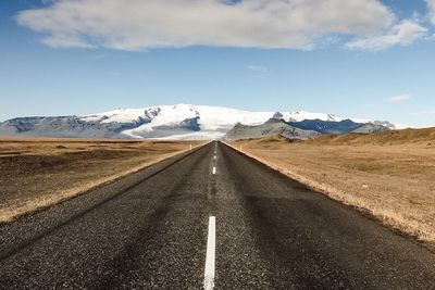 Road passing through field against cloudy sky