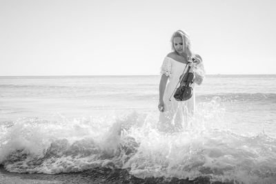 Beautiful woman holding violin while standing in sea at beach