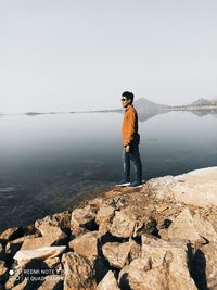 Man standing on rock by lake against sky