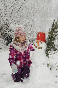 Girl with snowman on field against bare tree