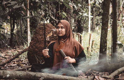 Full length of young woman holding plant in forest