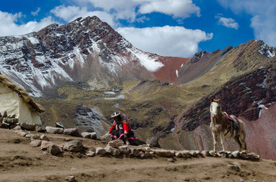 Rear view of woman in traditional clothing with horse sitting by mountains against sky