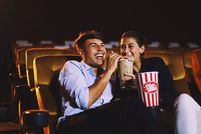 Happy couple having drink while sitting in movie theater
