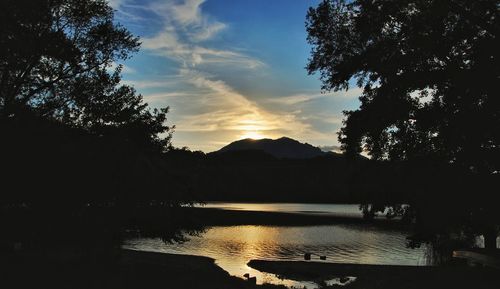 Silhouette trees by lake against sky during sunset