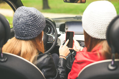 Trendy girls sitting in the car. teen in front of the steering wheel, friend using smartphone beside