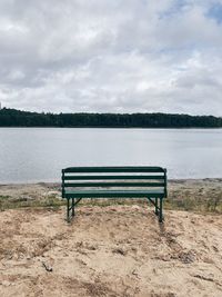 Empty bench by lake against sky