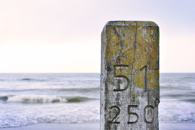 Text on wooden post at beach against sky