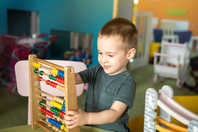 Smiling toddler boy playing with colourful toy abacus in a children's entertainment center