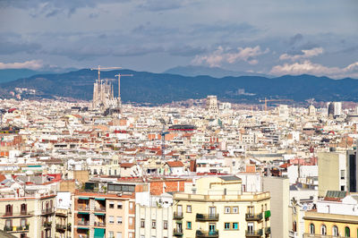 High angle view of townscape and silhouette of sagrada familia against sky, barcelona 